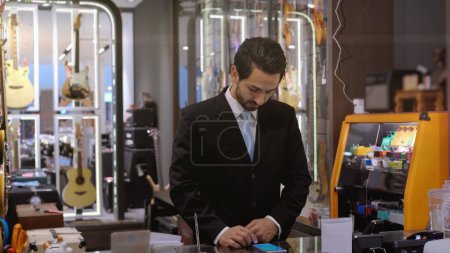 Photo for An upwardly mobile Middle Eastern man using a mobile phone - smartwatch to purchase product at the point of sale terminal in a retail store with nfc identification payment for verification - Royalty Free Image