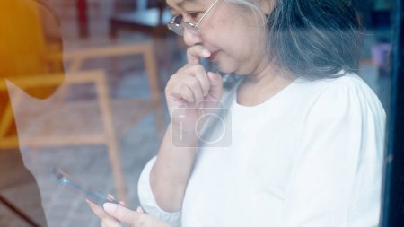 Téléchargez les photos : Femme d'affaires asiatique retraitée active aime travailler sur sa propre petite entreprise en ligne et se détendre dans un coffeeshop par une journée ensoleillée - en image libre de droit