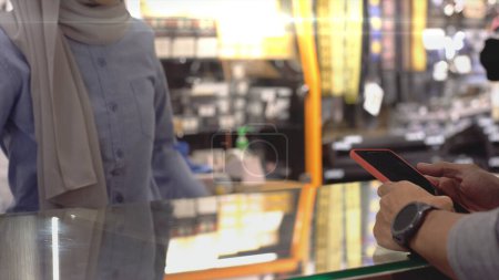 Foto de Un musulmán asiático ascendentemente móvil que usa un reloj inteligente para pagar un producto en una terminal de venta con código QR, pago de identificación nfc para verificación y autenticación - Imagen libre de derechos