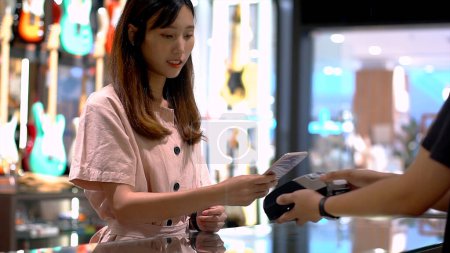 Foto de Mujer asiática joven que utiliza el teléfono móvil - smartwatch para comprar el producto en el punto de venta terminal en una tienda al por menor con cerca de campo de comunicación nfc identificación por radiofrecuencia de pago - Imagen libre de derechos