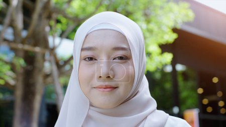 Foto de Acercamiento Retrato de una joven musulmana asiática vestida con el tradicional Hijab mirando con confianza y sonriendo a la cámara con la pared blanca como fondo - Imagen libre de derechos