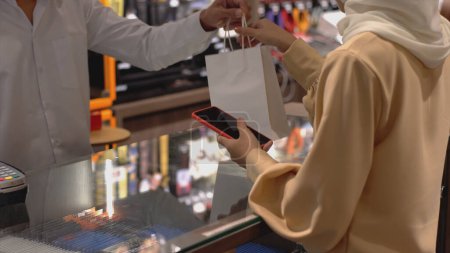 Foto de Una mujer musulmana asiática ascendentemente móvil que usa un teléfono móvil: smartwatch para pagar un producto en una terminal de venta con pago de identificación nfc para verificación y autenticación - Imagen libre de derechos