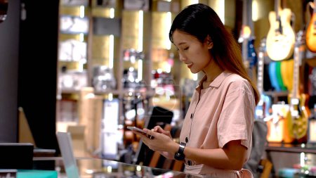 Téléchargez les photos : Jeune femme asiatique utilisant un téléphone mobile pour acheter un produit au terminal du point de vente dans un magasin de détail avec communication en champ proche technologie de paiement d'identification par radiofréquence nfc - en image libre de droit