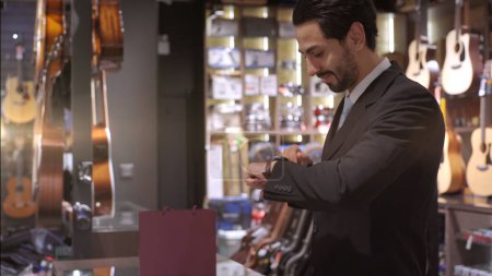 Téléchargez les photos : Un homme du Moyen-Orient qui se déplace vers le haut à l'aide d'un téléphone portable - smartwatch pour acheter un produit au terminal du point de vente dans un magasin de détail avec paiement d'identification nfc pour vérification - en image libre de droit