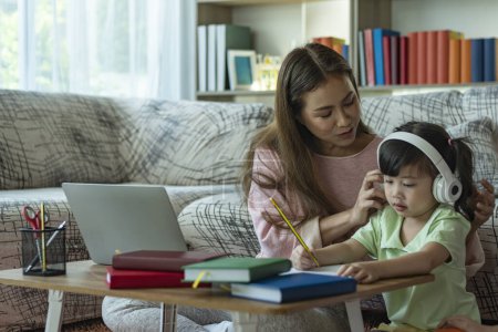 Téléchargez les photos : Une belle mère asiatique occupée à travailler tout en s'occupant de ses enfants et leur enseignant sur un ordinateur portable à la maison - en image libre de droit