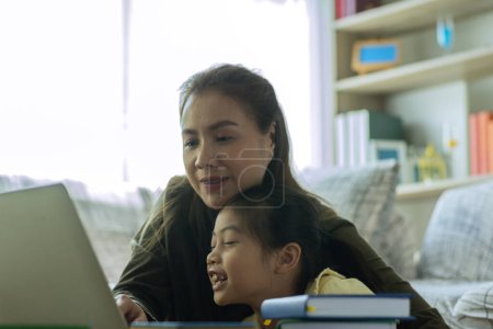 Téléchargez les photos : Une belle mère asiatique occupée à travailler tout en s'occupant de son enfant et en l'enseignant sur un ordinateur portable à la maison - en image libre de droit