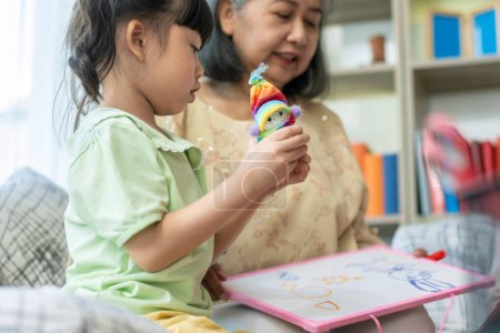 Photo for A kind and gentle Asia grandmother teaching her granddaughter to read write and drawing on a white board at home - Royalty Free Image
