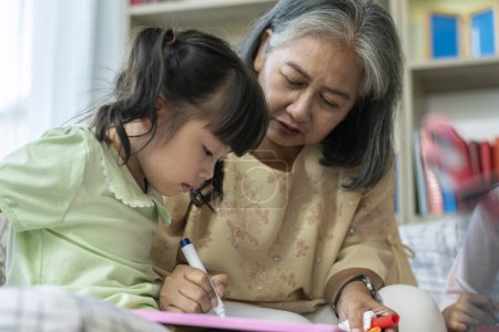 Photo for A kind and gentle Asia grandmother teaching her granddaughter to read write and drawing on a white board at home - Royalty Free Image