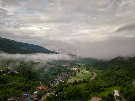 Foto de Vista aérea de un pueblo en la exuberante nube de lluvia verde cubre la montaña tropical de la selva tropical durante la temporada de lluvias en el parque nacional reservado Doi Phuka Mountain en el norte de Tailandia - Imagen libre de derechos