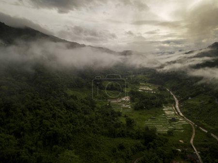 Foto de Vista aérea de un pueblo en la exuberante nube de lluvia verde cubre la montaña tropical de la selva tropical durante la temporada de lluvias en el parque nacional reservado Doi Phuka Mountain en el norte de Tailandia - Imagen libre de derechos