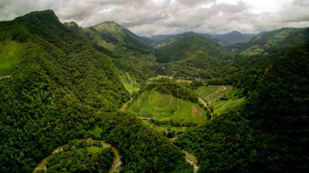 Vista aérea de un pueblo en la exuberante nube de lluvia verde cubre la montaña tropical de la selva tropical durante la temporada de lluvias en el parque nacional reservado Doi Phuka Mountain en el norte de Tailandia