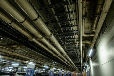Photo for Pipelines in the underground parking of a petroleum and gas refinery run along the ceiling, servicing the industrial complex - Royalty Free Image