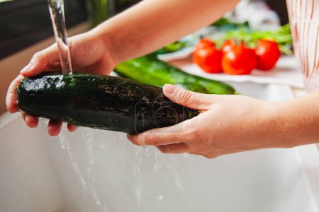 Foto de Las manos de la mujer lavando verduras, calabacín bajo el grifo de la cocina - Imagen libre de derechos