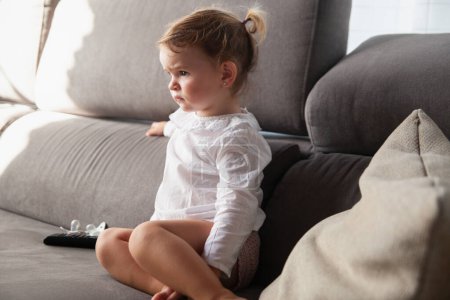 Foto de Retrato de una niña con chupetes en el lado sentado en el sofá viendo la televisión. - Imagen libre de derechos