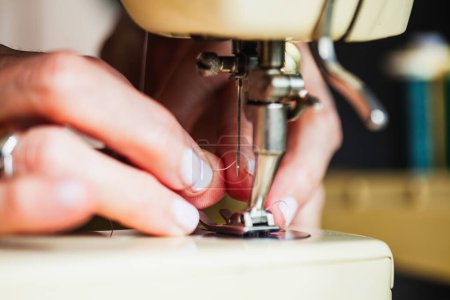 Photo for DETAIL OF A WOMAN'S HANDS THREADING THE NEEDLE OF THE SEWING MACHINE - Royalty Free Image