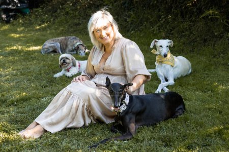 Foto de Mujer relajada sentada en el jardín sonriendo con sus cuatro mascotas - Imagen libre de derechos