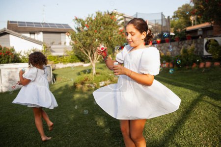 Foto de Chicas alegres jugando en el jardín con burbujas de jabón en verano - Imagen libre de derechos