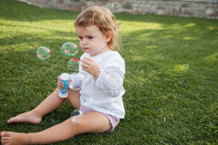 Photo for Baby girl concentrating on the soap bubbles playing in the garden - Royalty Free Image