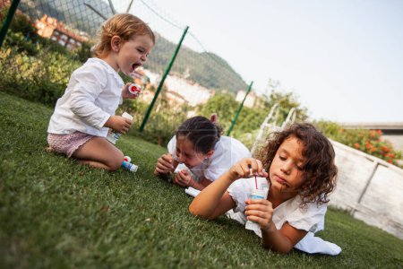 Foto de Tres niñas jugando en el patio con burbujas de jabón - Imagen libre de derechos