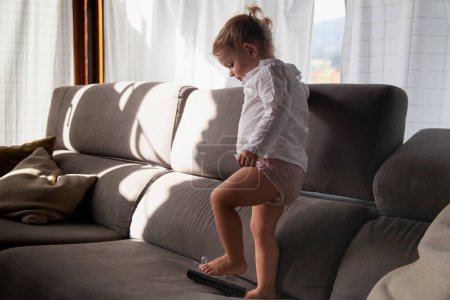 Photo for Baby girl playing on the sofa entertaining with the tv remote control - Royalty Free Image