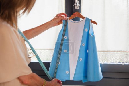 Photo for Dressmaker taking the measurements of a small handmade dress - Royalty Free Image