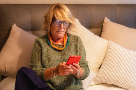 Foto de Mujer mayor sentada concentrada en contestar mensajes de teléfono móvil - Imagen libre de derechos