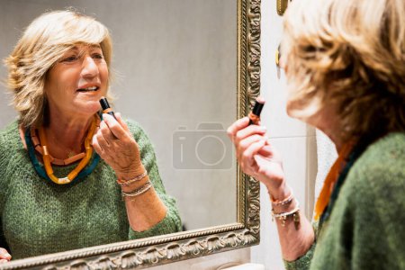 Téléchargez les photos : Femme mûre faisant ses lèvres devant le miroir de salle de bain - en image libre de droit
