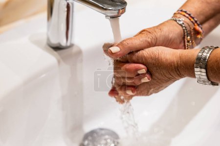 Foto de Mujer madura limpiándose las manos con agua en el baño - Imagen libre de derechos