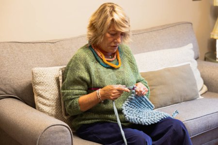Photo for Woman sitting on the sofa knitting and enjoying her hobby - Royalty Free Image