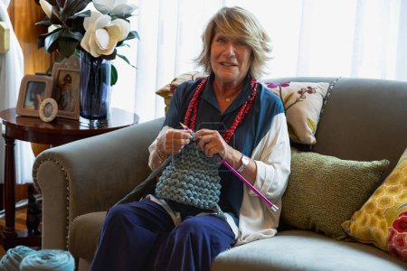 Photo for Older woman smiling and happy enjoying the hobby of knitting with her hands. - Royalty Free Image