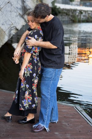Téléchargez les photos : Couple de mariés modernes embrassant sur une passerelle au bord de la rivière dans la ville - en image libre de droit