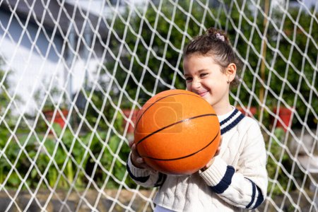 Téléchargez les photos : Portrait de petite fille souriant regardant la caméra avec basket dans la cour arrière à la maison - en image libre de droit