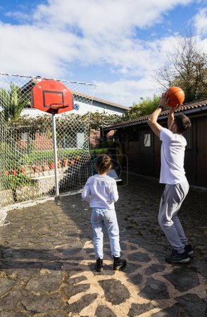 Photo for Father playing basketball with his daughter, throwing a shot to put it in the basket, vertical photo - Royalty Free Image