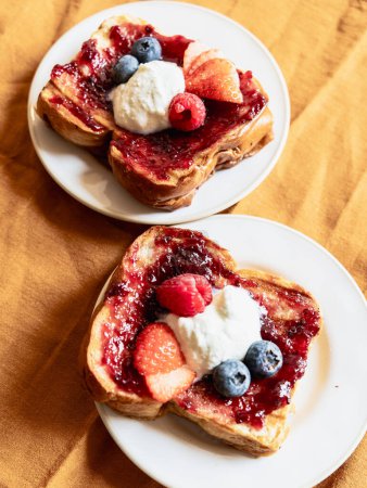 Photo for Close-up of two brioche toasts with jam and berries plus blueberries, vertical photo - Royalty Free Image