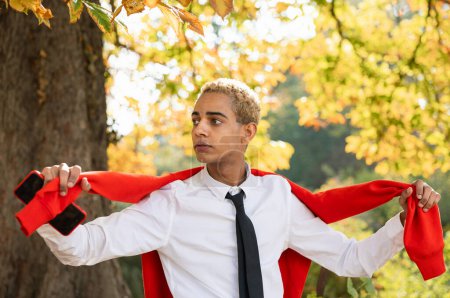 Téléchargez les photos : Portrait de beau jeune homme dans le parc avec pull rouge relaxant en profitant de la nature - en image libre de droit
