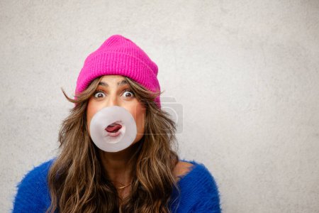 Photo for Close-up of an amused and surprised woman with a big bubble gum bubble.White space - Royalty Free Image