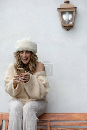 Foto de Mujer sentada en el porche en vestido de moda con gorra de pelo que se divierten interactuando con el teléfono celular, espacio de copia - Imagen libre de derechos