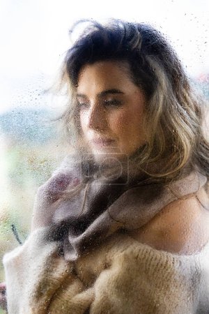 Photo for Portrait of a woman behind the glass window on a rainy day in the countryside, blank space - Royalty Free Image