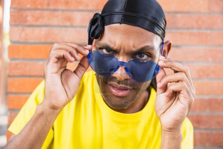 Téléchargez les photos : Jeune homme noir avec des lunettes de couleur avec une expression surprise en regardant la caméra, espace blanc - en image libre de droit