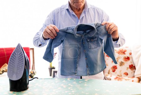Foto de Hombre mayor retirado clasificando la ropa que está planchando en casa - Imagen libre de derechos
