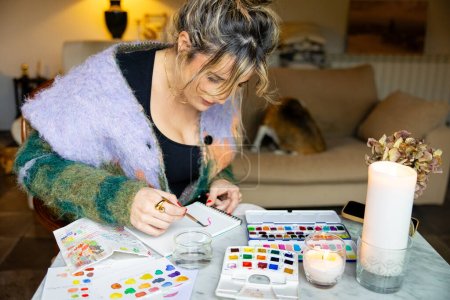 Téléchargez les photos : Photo de jeune femme à la maison appréciant peindre des aquarelles à la maison en détente - en image libre de droit