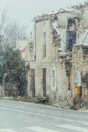 Téléchargez les photos : Détail d'une maison rurale à côté de la route à moitié détruite couverte de neige, photo verticale - en image libre de droit