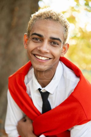 Foto de Retrato de un joven sonriente con el pelo rubio rizado y una bufanda roja sobre sus hombros, exudando optimismo y confianza. - Imagen libre de derechos