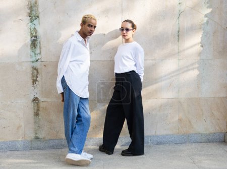 Téléchargez les photos : Un jeune homme et une jeune femme se dressent avec confiance contre un mur texturé, présentant leurs tenues monochromes et leurs chaussures à la mode. - en image libre de droit