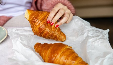 Photo for Woman's hand with red nails grabbing a golden-baked croissant, symbolizing a fresh morning start. - Royalty Free Image