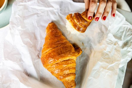 Photo for Close-up of a freshly baked croissant being picked up, highlighting the flaky texture and golden crust. - Royalty Free Image