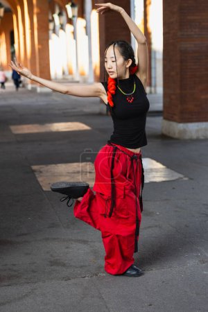 Téléchargez les photos : Une danseuse urbaine en pantalon rouge saisissant exécute une pose élégante inspirée par la danse orientale sur une passerelle de ville. - en image libre de droit