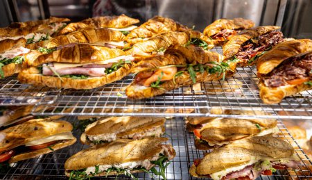 Foto de Una variedad de sándwiches de croissant y focaccia recién preparados con deliciosos rellenos presentados en una tienda de delicatessen. - Imagen libre de derechos