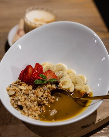 Foto de Cuenco de granola nutritivo rematado con plátanos en rodajas, fresas y una llovizna de miel, perfecto para un desayuno saludable. - Imagen libre de derechos