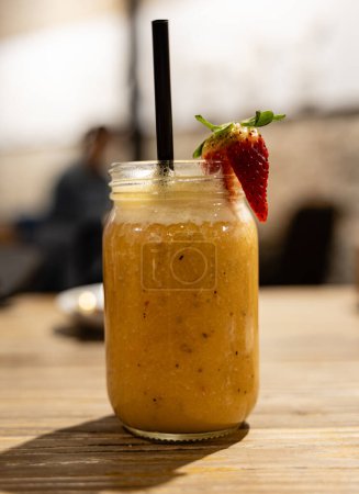 Photo for A refreshing fruit smoothie garnished with a ripe strawberry, served in a mason jar on a rustic wooden table. - Royalty Free Image
